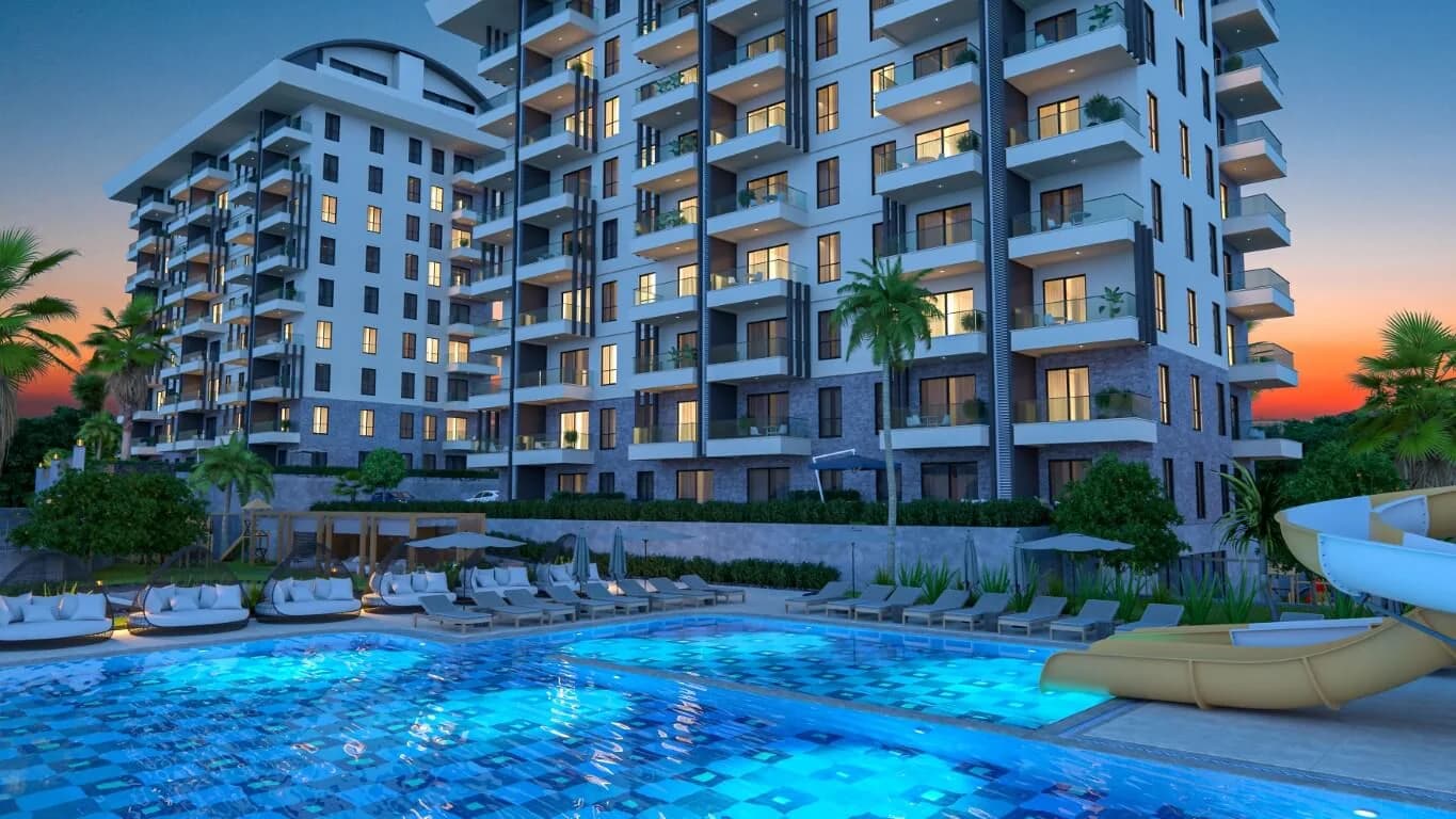 Luxury apartments for sale in Payallar showing the Konak Towers outdoor swimming pool, water slide, and modern building exterior at sunset.